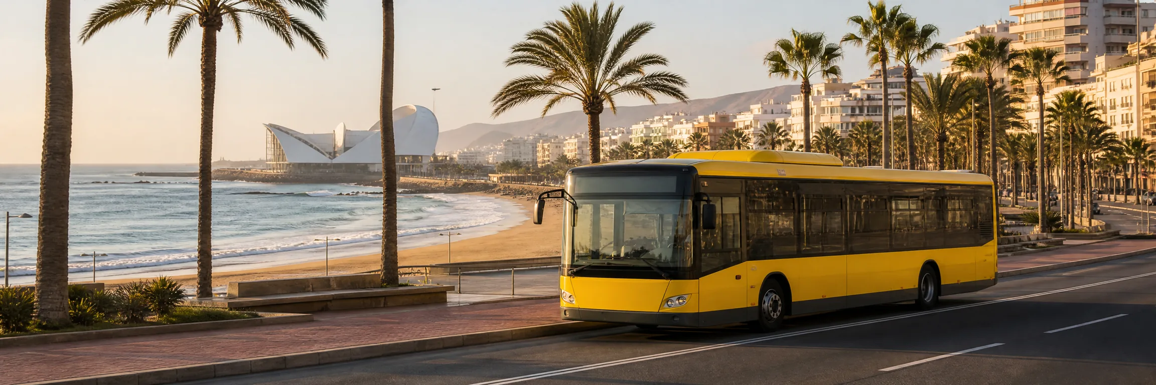 Guagua urbana amarilla de Guaguas Municipales en el paseo marítimo de Las Palmas de Gran Canaria, con Las Canteras y el Auditorio al fondo